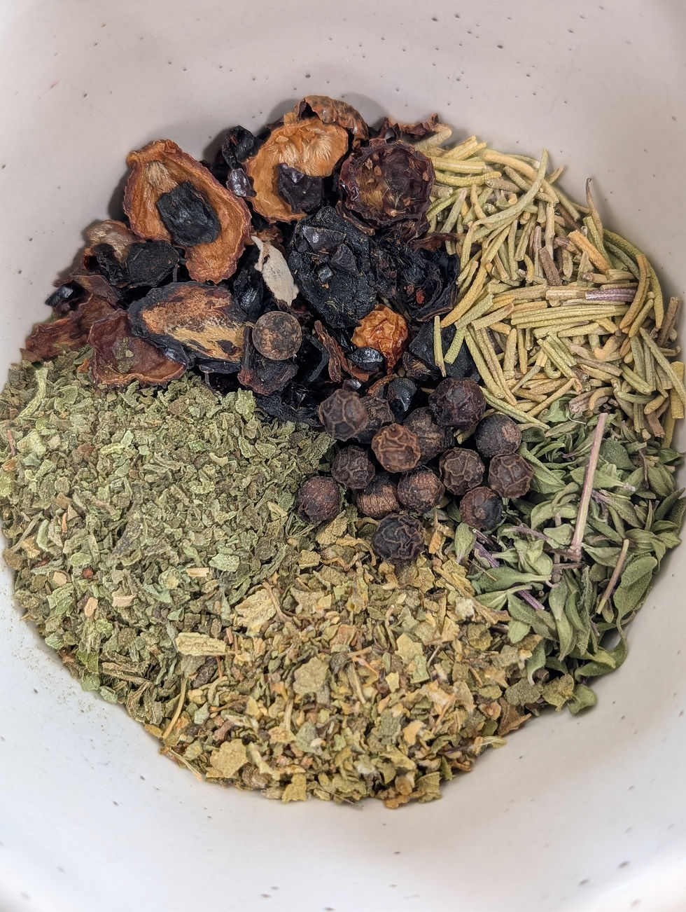 Dried herbs, shot from above, in the bowl: rosemary, peppercorns, thyme, oregano, rosehips, basil