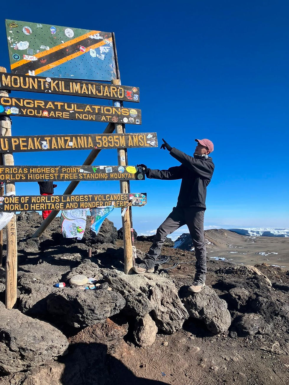 A man standing and pointing at the sign at the top of Kilimanjaro
