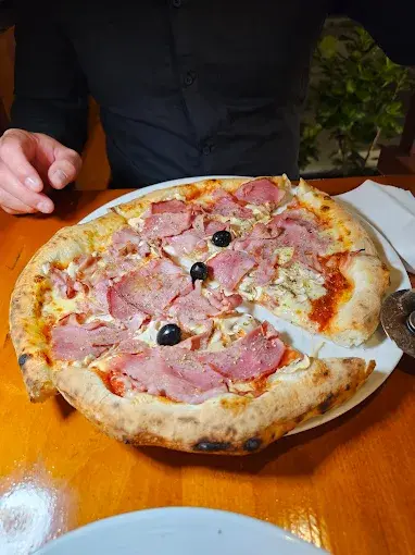 Close-up of Ham pizza on a wooden table at Tudors in Split.