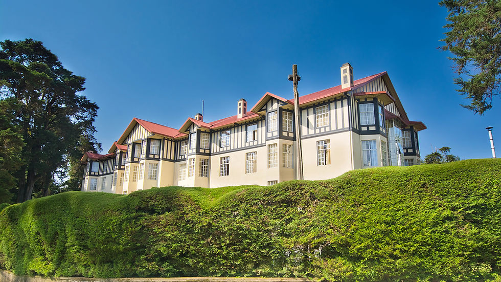 a colonial Tudor style hotel building against a blue sky and behind a tall hedge