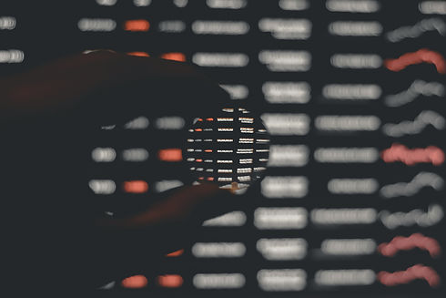 Hand holding a magnifying glass over a digital screen showing numbers and words signifying technology.