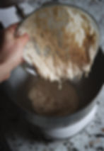 Hand pouring sticky starter dough from a glass bowl into a metal mixer on a speckled countertop.