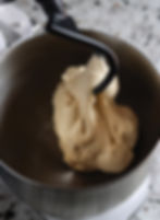 Dough being kneaded by a dough hook in a stand mixer bowl. The beige dough contrasts with the metallic bowl against a speckled countertop.
