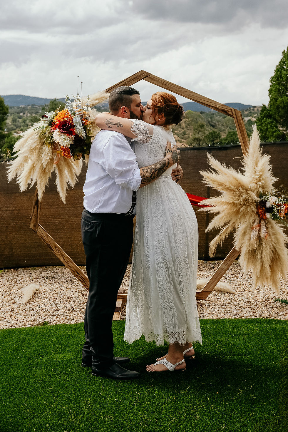 Bride and groom kiss beneath a wooden wedding arch during an intimate outdoor wedding in Prescott, Arizona.