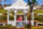 Woman posing inside a white gazebo surrounded by colorful flowers during an outdoor portrait session.