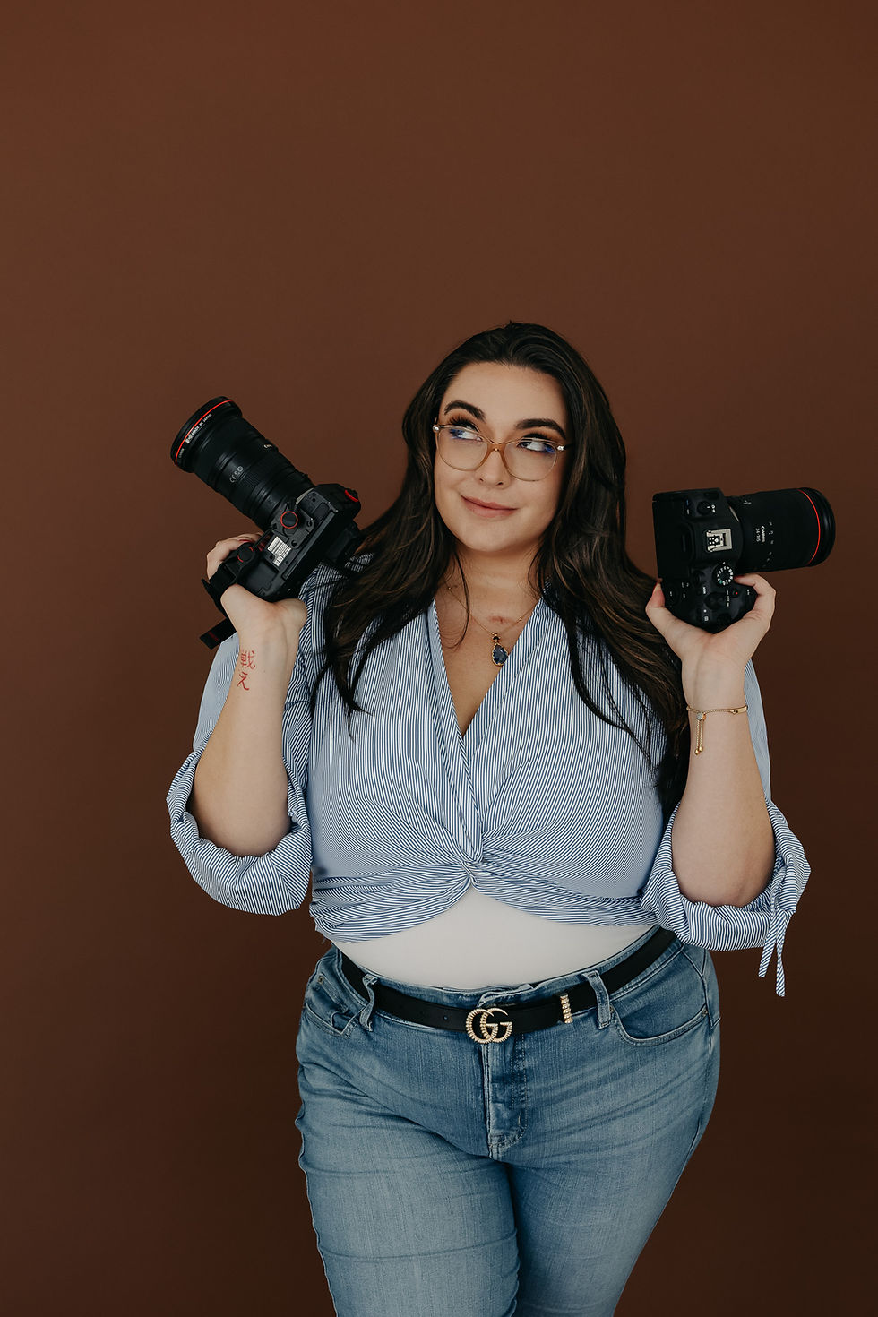TaylorTigerlily Photography owner and creative director Taylor holding two professional cameras in a studio portrait in San Diego, California.