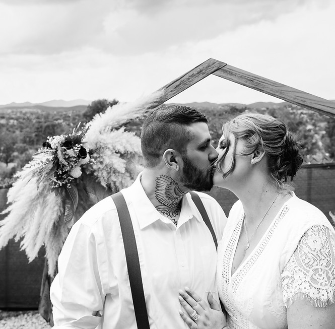 Black and white portrait of a newlywed couple kissing beneath their wedding arch in Prescott, Arizona.