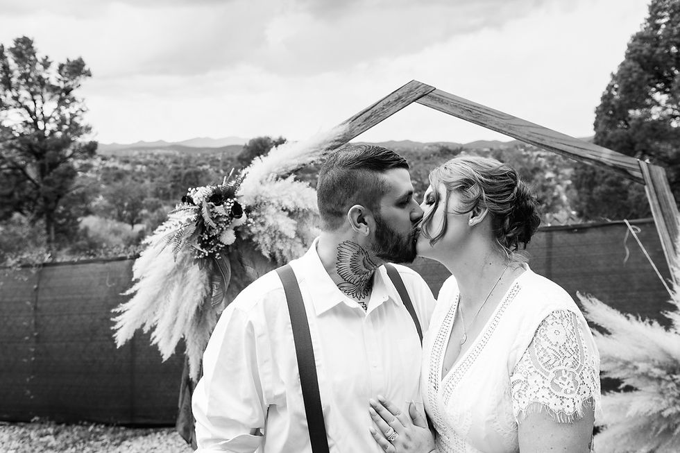 Black and white portrait of a newlywed couple kissing beneath their wedding arch in Prescott, Arizona.