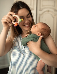 A mother holding and playing with a rattle with her newborn