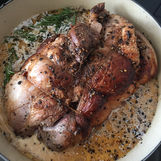 Trussed and seared pork with whole black peppercorns and rosemary braising in liquid in a large pot. Juicy and browned with herbs visible, creating a warm and savoury atmosphere. The setting is a stove top.
