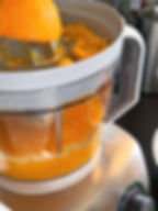 Orange being juiced in a silver electric juicer. Fresh juice fills the transparent container. Bright, vibrant colors in kitchen setting.