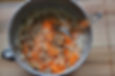 Mixing bowl with grated carrots and walnuts on pancake batter, spoon inside, on a wooden surface. Earthy colors suggest baking preparation.