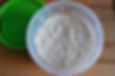 Bubbly sourdough starter in a clear container on a wooden surface; a green lid is nearby. The texture is light and airy.