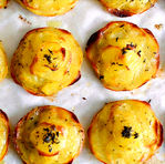 Golden potato stacks with herbs on parchment paper, baked to a crispy finish. Each piece is topped with green herbs creating a rustic look.