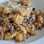 Gnocchi with sausage and porcini sauce with grated cheese on a white plate. The dish has a rustic look with a creamy, appetizing texture.