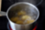 Potatoes boiling in a stainless steel pot on a stovetop. Bubbles form on the surface of the water, with steam rising.