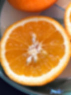 Close-up of a sliced orange on a plate, showing juicy segments and seeds. Bright orange and white colors stand out against a dark background.