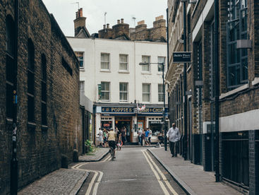 Shadowed London street with naturally lit white buildings in background. People can be seen walking.i