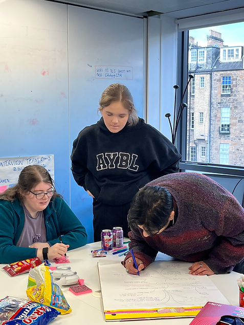 Three YouthVIP panel members work together on a task. One is writing on a piece of flipchart paper, writing down their ideas, as they share insights.