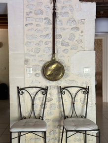Décoration authentique du Domaine du Bardon : chaises en fer forgé et poêle ancien sur mur en pierre, gîte de charme en Charente-Maritime pour un séjour rustique et chaleureux.