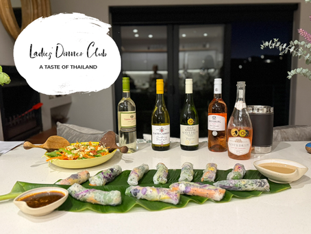 Summer rice rolls and Thai cashew veg salad on a table with five wine bottles, an ice bucket, and dipping sauces. Text reads: Ladies Dinner Club, A Taste of Thailand.