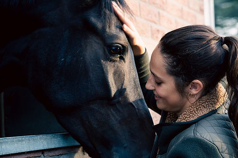 Une jeune femme qui caresse la tête d'un cheval et qui le regarde avec amour