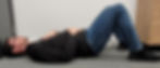 A man lying on his back with one hand on his chest and one hand on his tummy. His belly is pushed out for breathing in.
