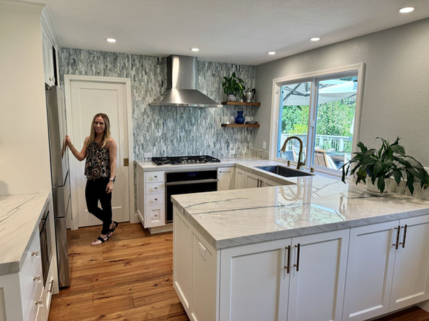 Woman in kitchen with white cabinets, silver range, and wooden floors.