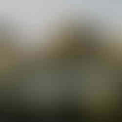 Aerial drone view of wedding guests mingling during cocktail hour, standing in small groups across an outdoor venue, holding drinks and chatting in a relaxed, festive atmosphere.