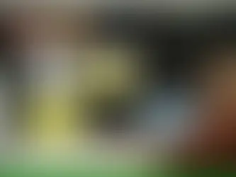 Man with glasses in an office cubicle on a video call. Wall displays SWOT analysis and charts. Desk has papers and a coffee cup.