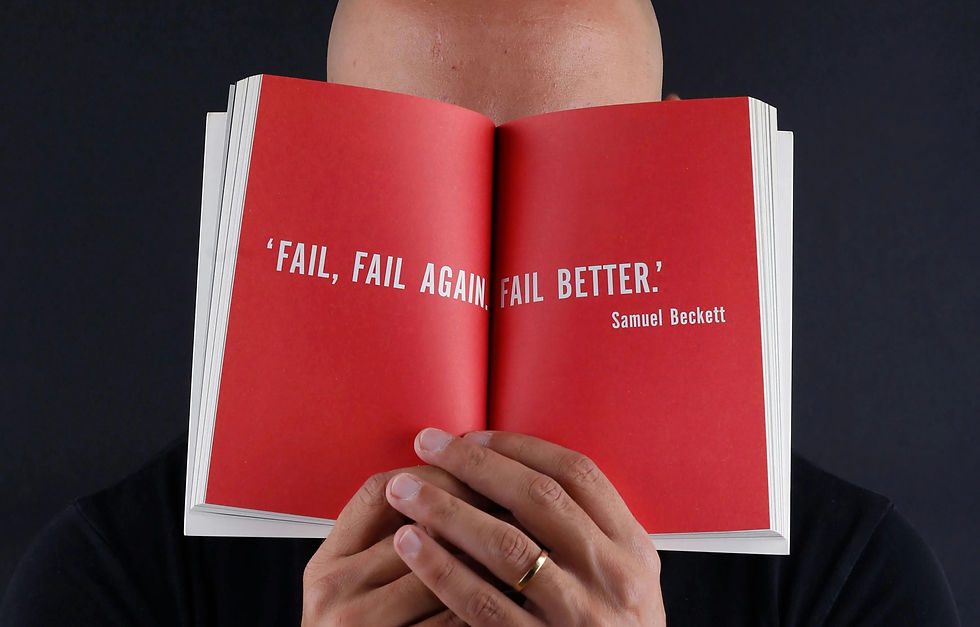 Bald person holding open a red book with the text, 'FAIL, FAIL AGAIN, FAIL BETTER.' by Samuel Beckett. Dark background, contemplative mood.