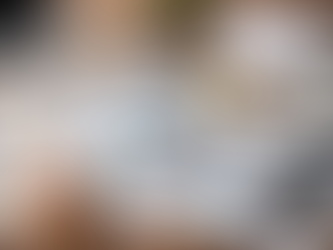 A high-resolution photo of a wooden desk set up for a monthly financial audit, featuring printed financial reports with colorful pie charts and bar graphs, a clipboard with budget documents, a magnifying glass placed over a chart, a calculator, a silver analog alarm clock, a desk calendar with check marks, a stack of cash, a laptop in the background, and a hand writing in a checklist notebook.