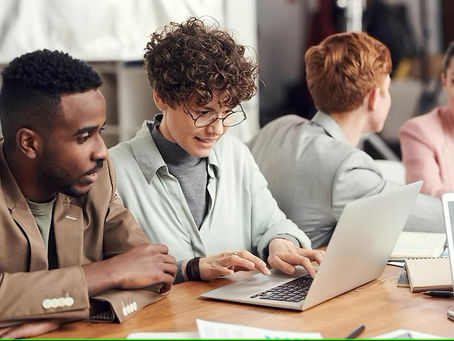 Colleagues in an office setting, smiling and collaborating at a table with laptops and notebooks, showcasing teamwork and focus.