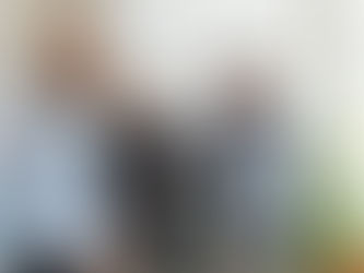 Three professional men in an office setting discussing financial strategy. One man in a light blue shirt holds US dollar bills while looking at a whiteboard with data charts, as his colleagues—one in a navy shirt with arms crossed and another in a striped shirt looking at a laptop—stand nearby, illustrating a collaborative business meeting or financial review.