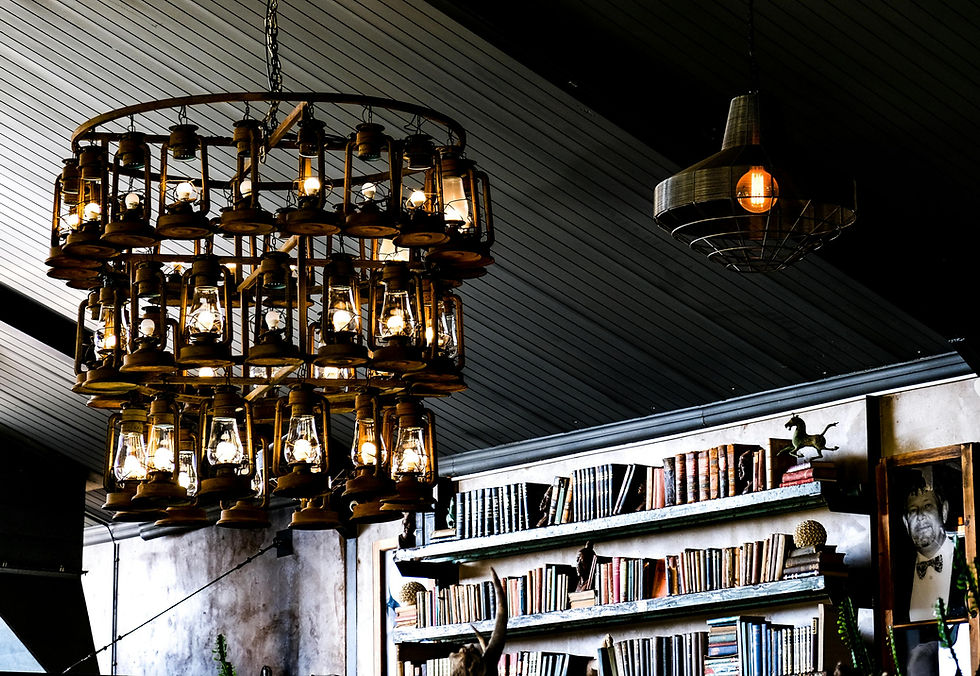A large, intricate chandelier made of vintage oil lanterns hanging in a dimly lit library, symbolizing "bright ideas" and the light of knowledge in development theory.