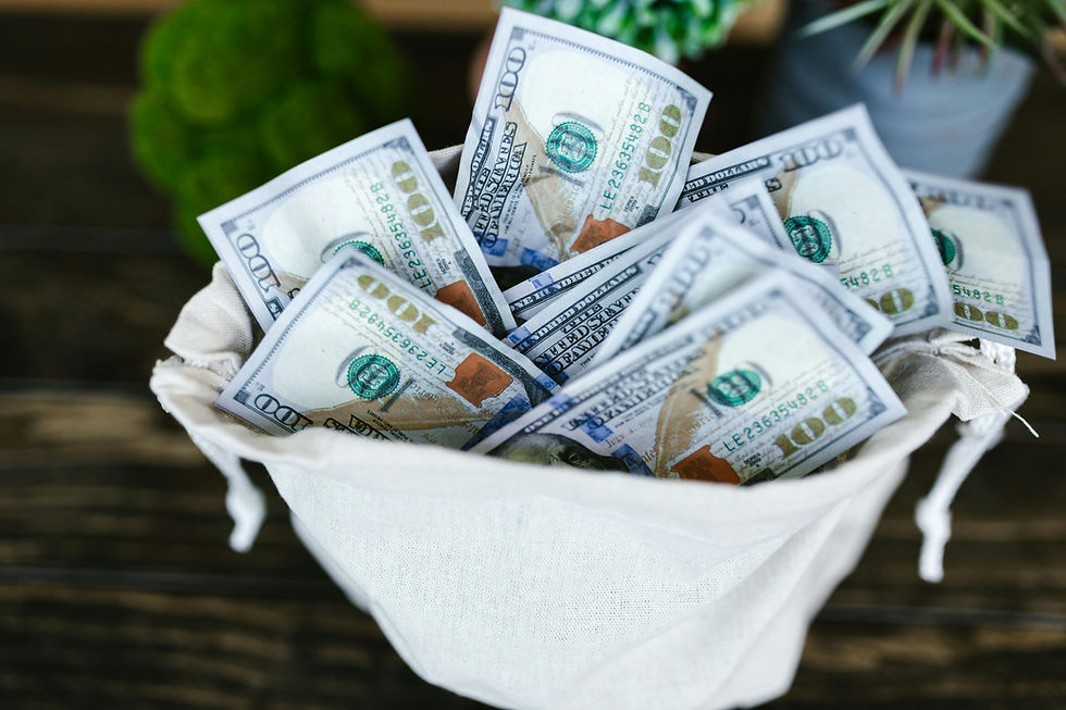 A beige sack overflowing with US $100 bills, set on a wooden surface. Green plants are blurred in the background, creating a rich mood.