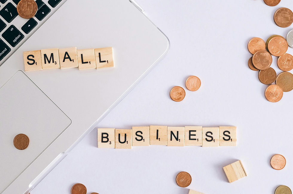 Wooden letter tiles spell "SMALL BUSINESS" on a laptop with scattered coins on a white background, creating a financial theme.