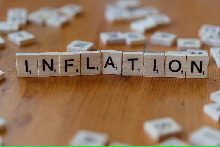 Wooden Scrabble tiles spell "INFLATION" on a brown table, surrounded by scattered tiles, conveying a theme of economic concern.