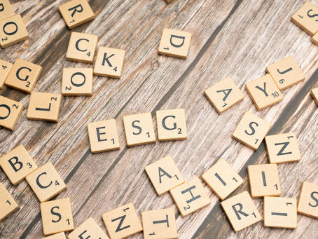 Scrabble tiles scattered on a wooden table spelling "ESG." Other random letters are visible, creating a playful, casual mood.