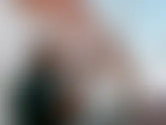 Man with megaphone shouts during a protest. Background shows a wall and sky. Others hold signs, enhancing a spirited atmosphere.