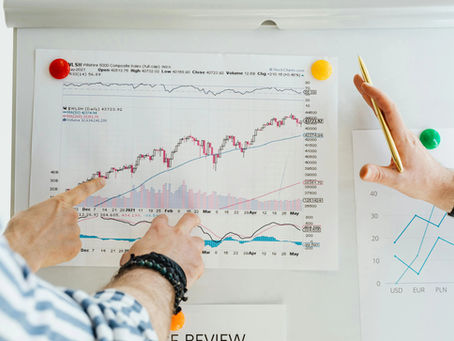 Two hands pointing at a stock market chart on a wall, one with a pen. Bright pins hold the chart. Visible emotions: focused analysis.