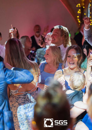 A crowd of happy guests cheer and dance on a packed dance floor at a lively party. Professional event photography by SGS Photography capturing the energy of the celebration.
