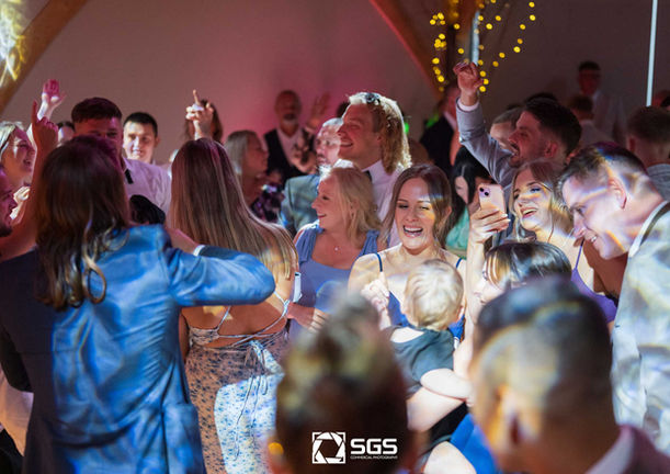 A crowd of happy guests cheer and dance on a packed dance floor at a lively party. Professional event photography by SGS Photography capturing the energy of the celebration.
