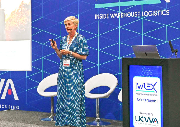Female presenter speaking at corporate event with IMLEX branded backdrop