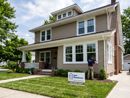 A professional window installer from Just Windows by Slocomb installing custom white vinyl replacement windows on a two-story home in Wilmington, Delaware, featuring a company yard sign in the front lawn.