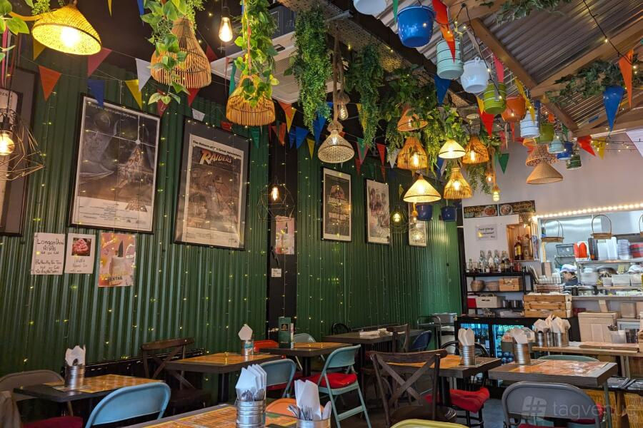 Cozy café with vibrant decor, green walls, hanging lights, and colorful flags. Empty tables set with napkins. Posters adorn the wall.