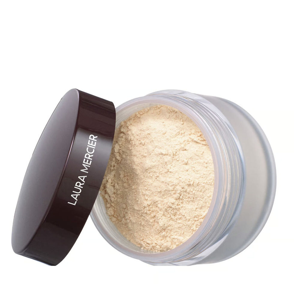 Open jar of beige powder with black lid displaying "Laura Mercier" text. The setting is a white background, focusing on cosmetic product.