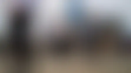 People walk on a busy city street with skyscrapers and cranes in the background. The mood is bustling under a partly cloudy sky.