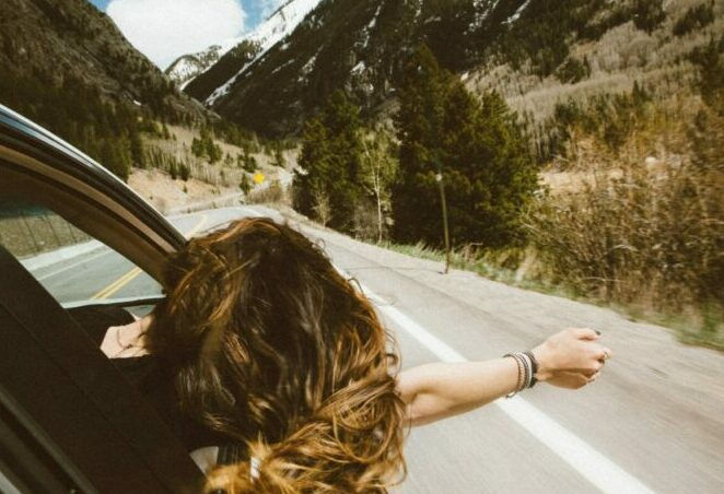 Woman in car leaning out the window with her arm, her hair blowing in the wind