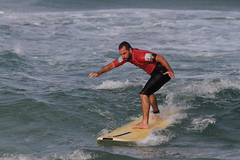 Imagem de um atleta com deficiência visual surfando. Ao fundo, o mar azul preenche a imagem.